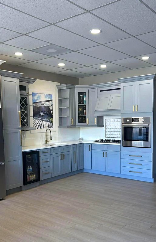Powder blue-gray shaker cabinets with brass pulls, lattice wine rack and glass display — on display at MNK Cabinet's Norcross, GA showroom