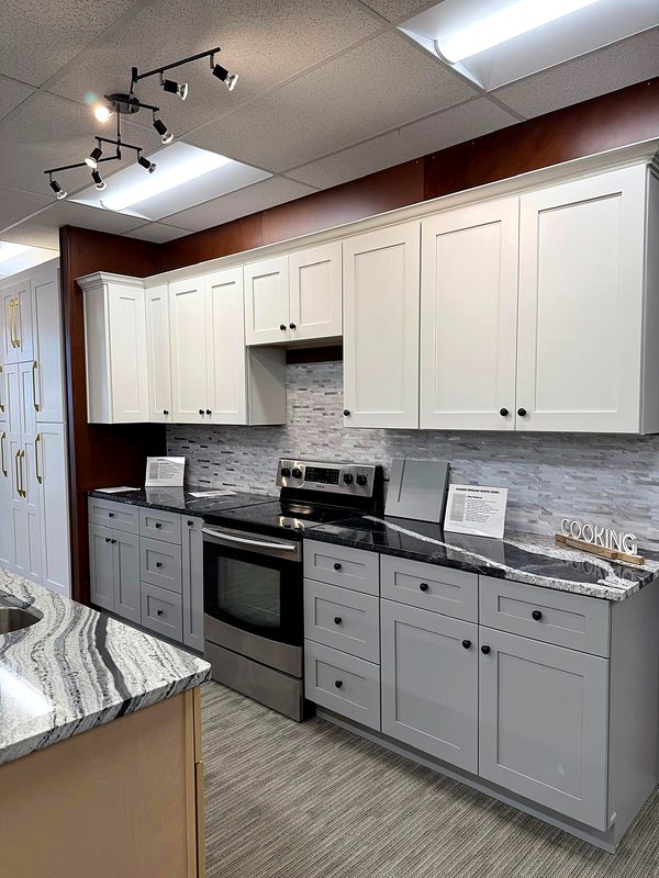 Cream/off-white shaker uppers with black knobs over light gray shaker base cabinets — on display at MNK Cabinet's Norcross, GA showroom