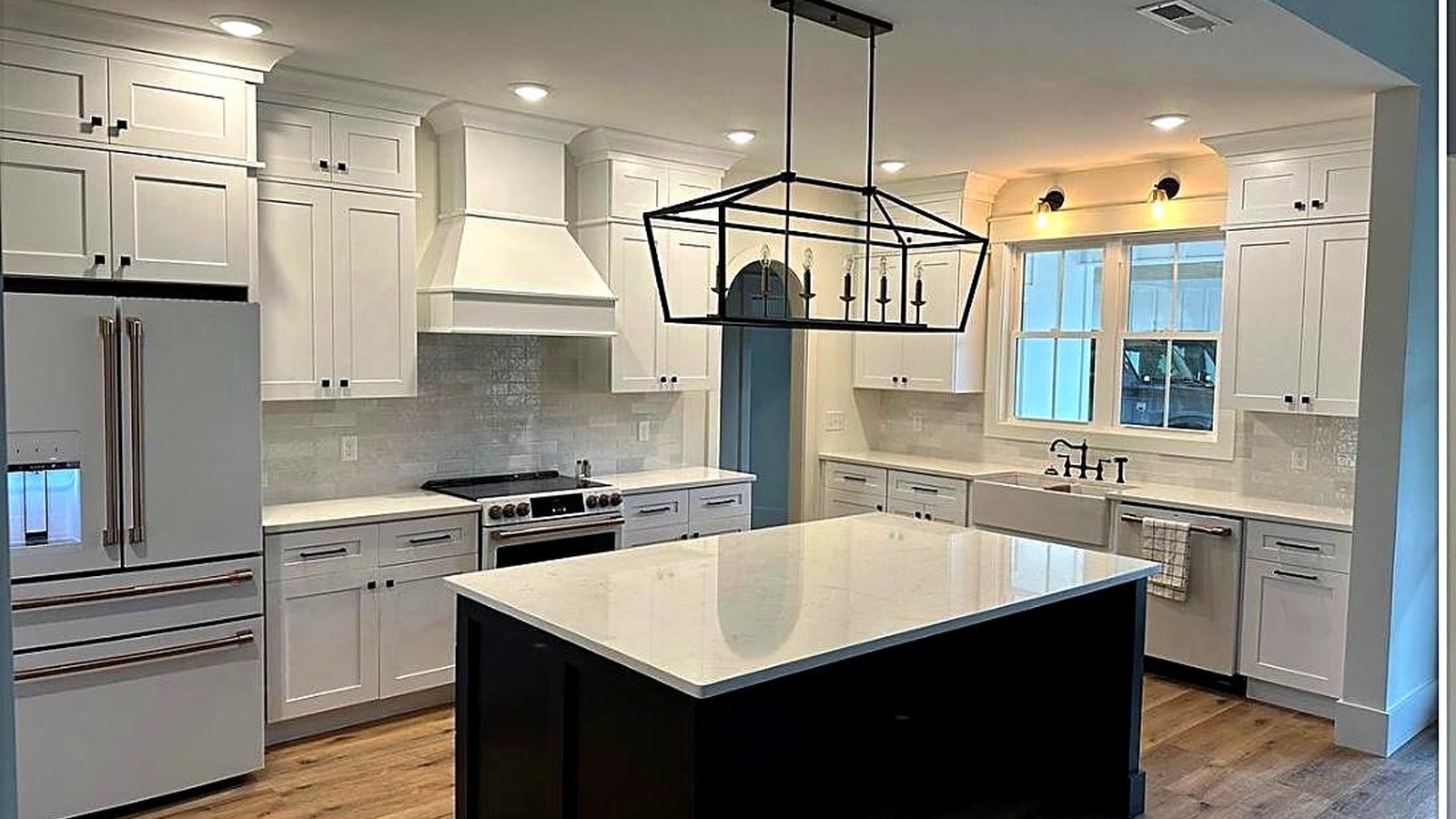 White shaker kitchen with a black island and farmhouse sink, the wet zone where cabinet finishes wear fastest