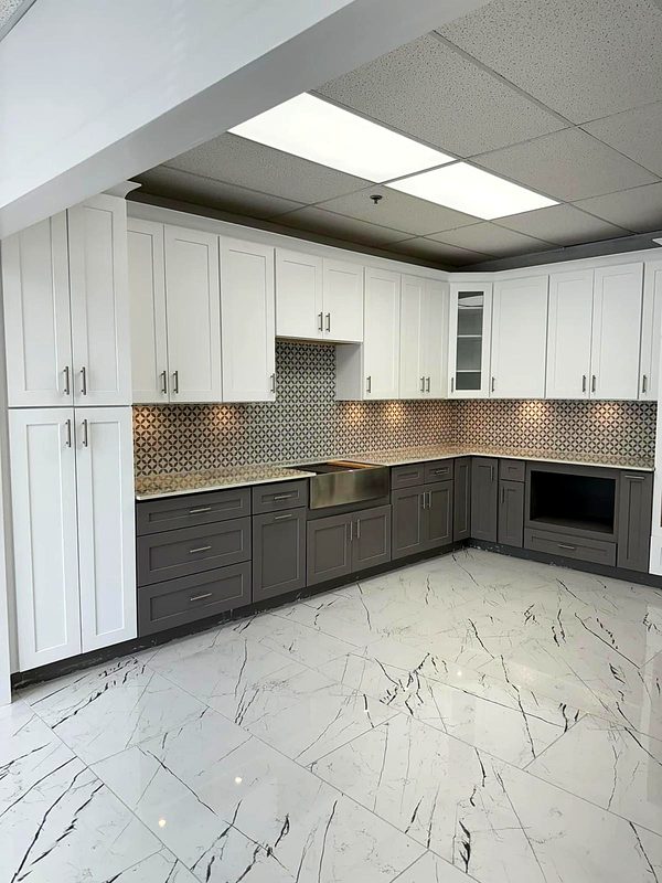 Two-tone L-shaped showroom kitchen: white shaker uppers and tall pantry with dark gray — on display at MNK Cabinet's Norcross, GA showroom