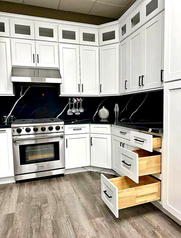 Bright white shaker cabinets with glass-front stacked uppers and matte black pulls — on display at MNK Cabinet's Norcross, GA showroom