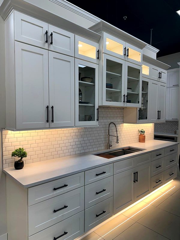 White shaker cabinets with lighted glass-front display uppers, matte black bar pulls — kitchen by MNK Cabinet in metro Atlanta