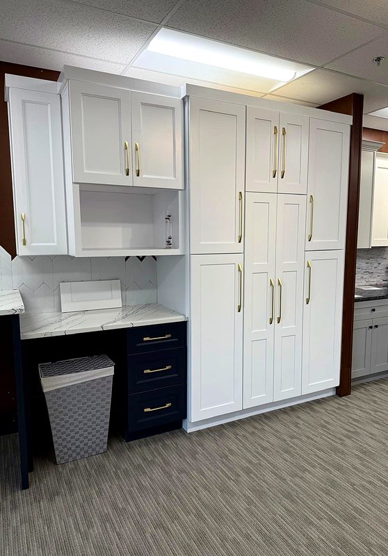 White shaker floor-to-ceiling pantry wall with long brass pulls next to a navy shaker — on display at MNK Cabinet's Norcross, GA showroom