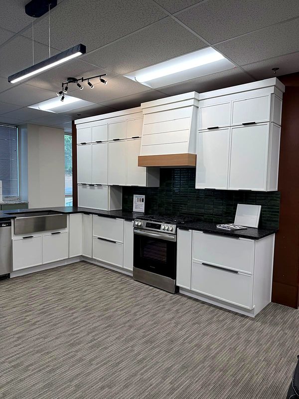 White slim-shaker cabinets with black pulls, white shiplap range hood with natural wood — on display at MNK Cabinet's Norcross, GA showroom
